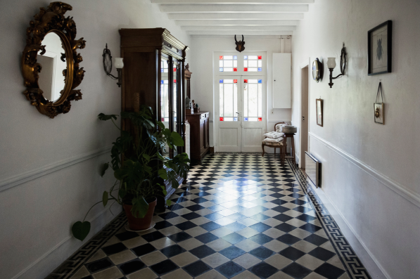 Image inside of a hallway leading to the front door of a house with a black and white squared pattern on the floor