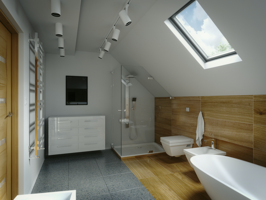 Contemporary loft bathroom with a sloped ceiling and large roof window providing natural light. The space features a freestanding bathtub, wall-mounted toilet, bidet, glass-enclosed shower, white vanity unit, wood-effect wall tiles, grey floor tiles, and modern ceiling spotlights, creating a bright and stylish attic bathroom.