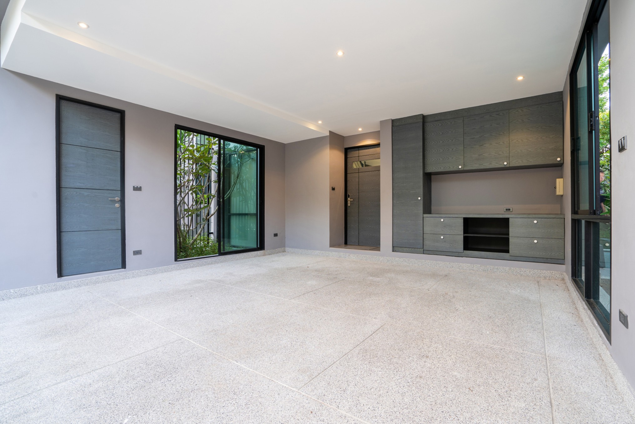 Contemporary converted garage interior featuring polished flooring, built-in storage cabinets, recessed ceiling lighting, large glazed doors and windows, and a modern open-plan living or workspace design.