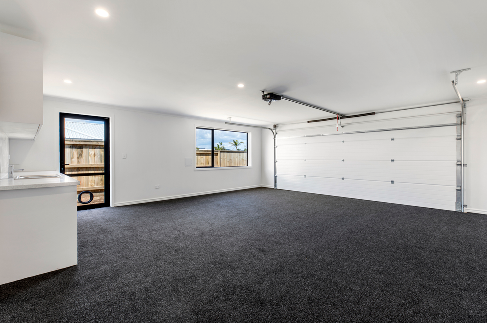 Converted garage transformed into a clean, multi-purpose living space featuring carpeted flooring, recessed ceiling lights, white walls, a side access door, large window, and retained insulated garage door.